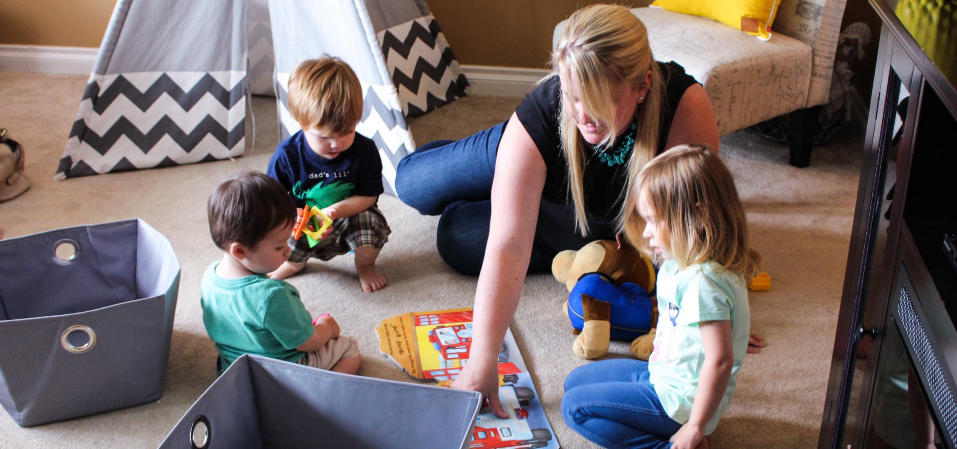 young blonde woman on carpet with three toddlers in home child care setting