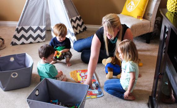 young blonde woman on carpet with three toddlers in home child care setting
