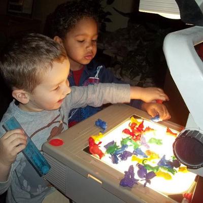 two young children putting plastic objects on a light table
