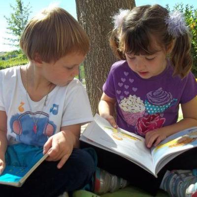 two children reading books side by side outside on the grass