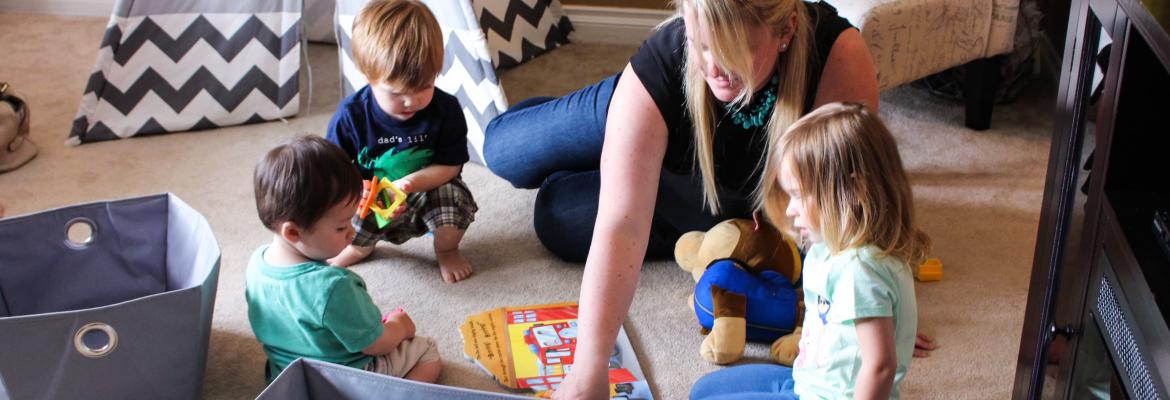 home child care provider and three children looking at a book on the carpet of a living room