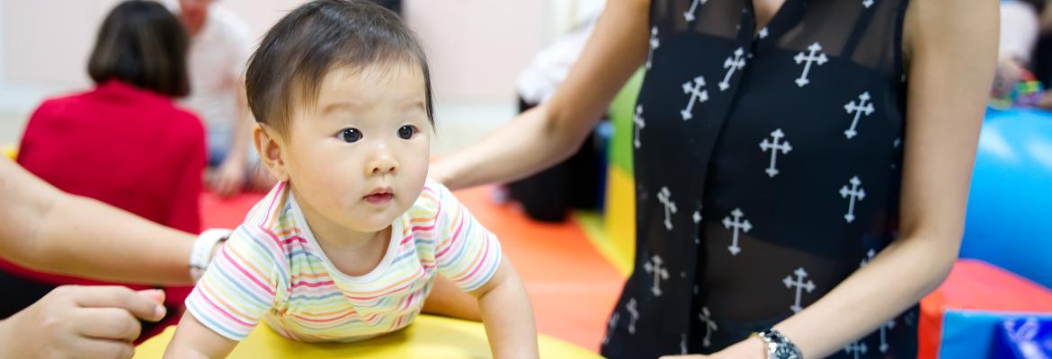 young infant age child balancing on a large soft ball with female adult supervision