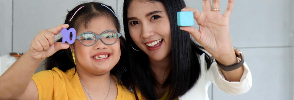 educator and child exploring differently shaped blocks and smiling at camera