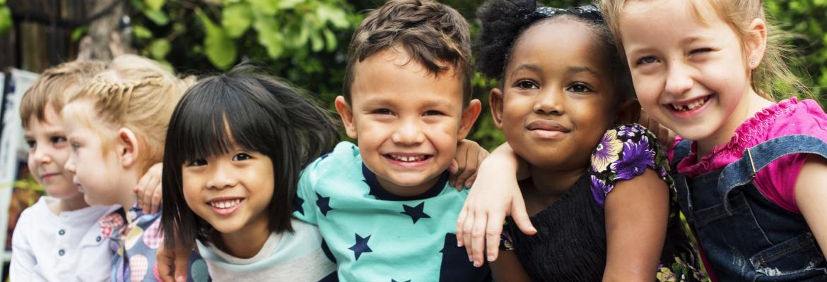 six multicultural children with arms around each other smiling at camera