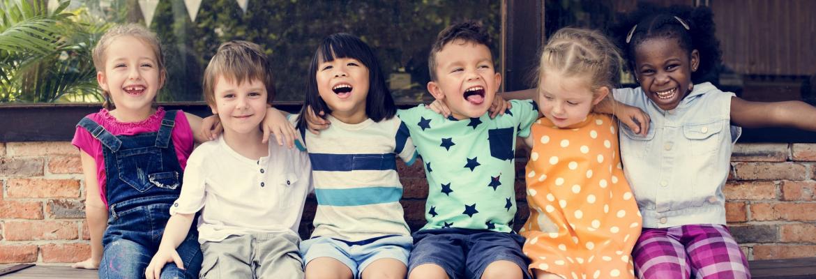 six multi-cultural children smiling at camera and sitting on a bench