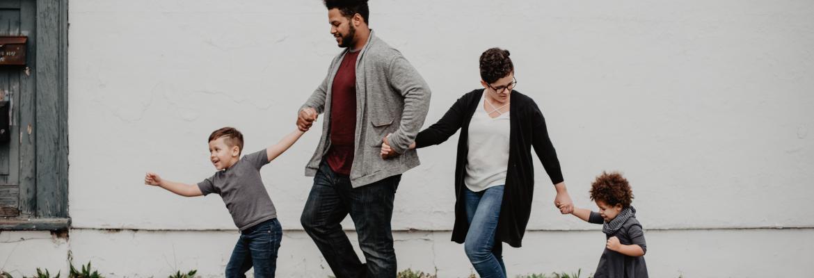 two parents and their two young children walk together outside on the sidewalk