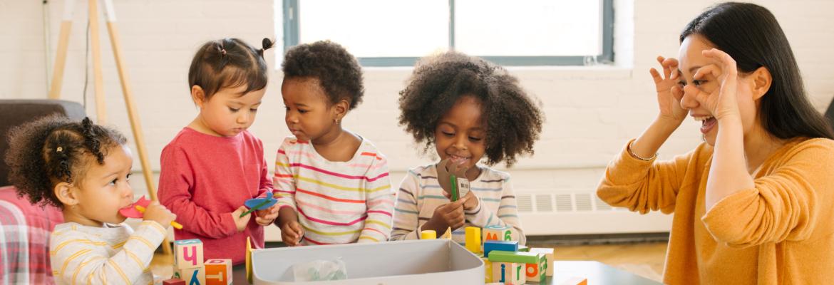 home child care provider and four young children of varied children playing with toys on top of a table